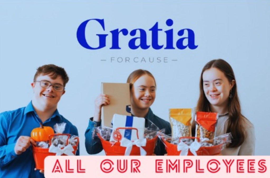 Three young adults with disabilities are smiling and holding gift baskets in front of a promotional backdrop for Gratia For Cause, which highlights their status as employees.